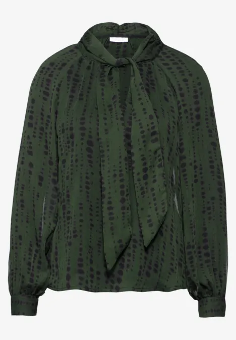 Grüne Bluse mit schwarzem Muster und Schleifenkragen.